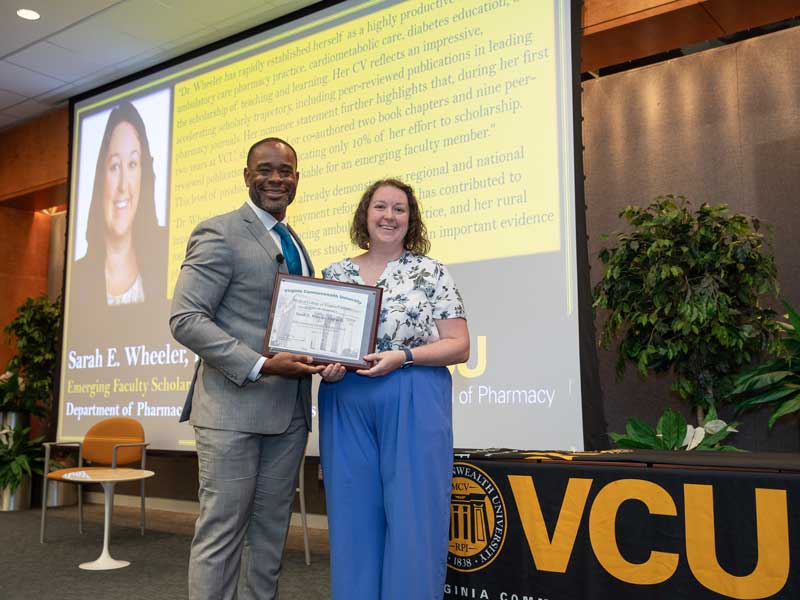 Standing onstage next to Dean K.C. Ogbonna, Sarah Wheeler, Pharm.D., accepts the Emerging Faculty Scholar Award