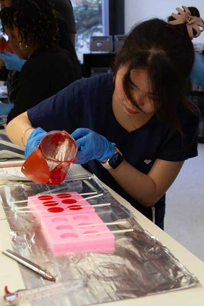 A student pours a medicated solution into a lollipop mold