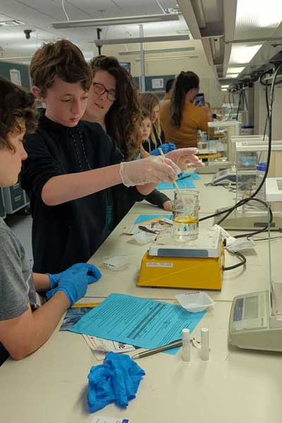 Students stir a solution in a lab while a professor looks on